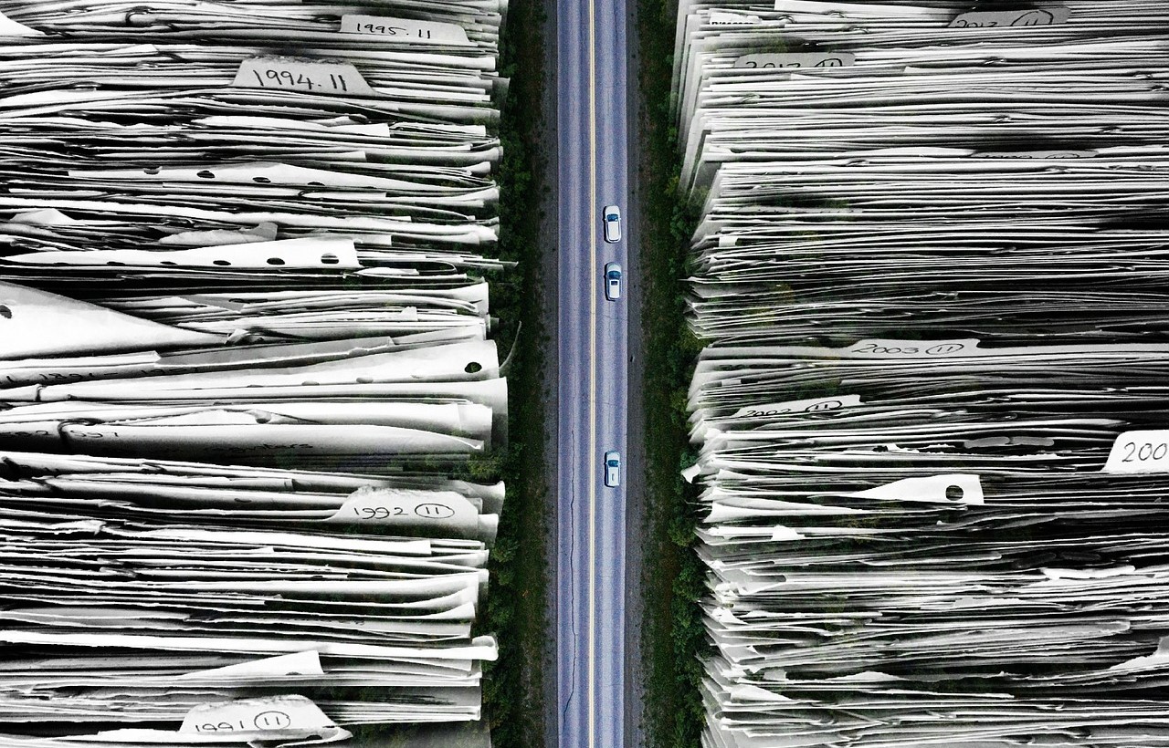 In the middle of the picture there is a highway on which cars are driving. On the both sides of the picture there are piles of paper.